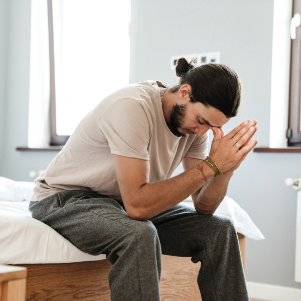 joven sentado en la cama en casa con tristeza, representando problemas de salud mental en hombre