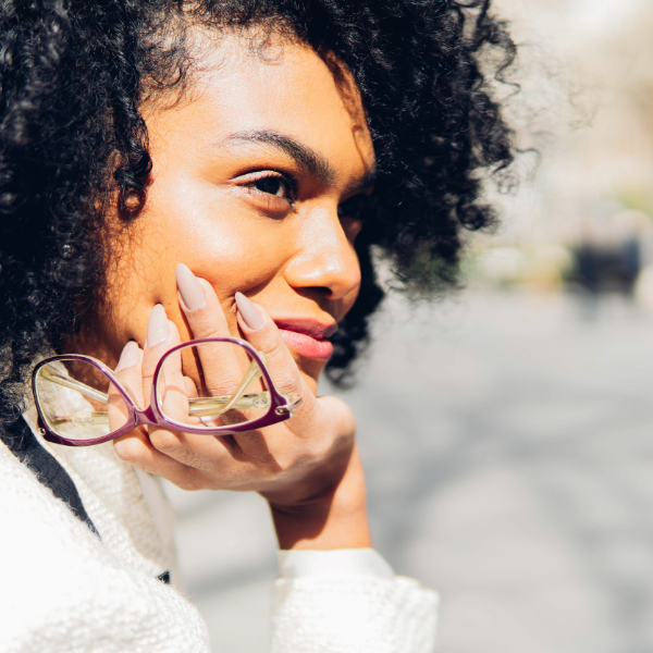 mujer sosteniendo unas gafas de sol frente con el sol como medida de protección ocular y la radiación solar