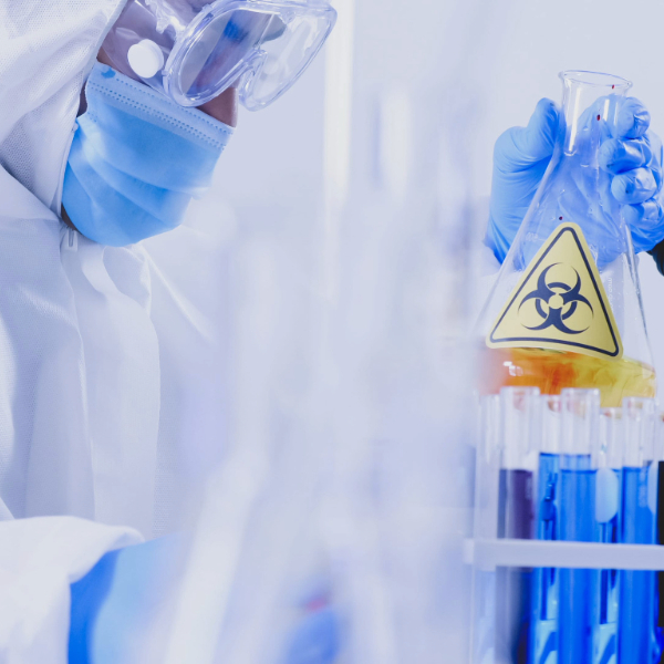 Trabajador de laboratorio con elementos de protección analizando un líquido en un tubo de ensayo, como ejemplo de los tipos de peligros laborales en el trabajo