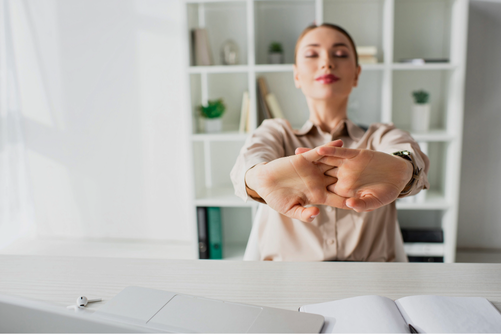 mujer realizando estiramientos de manos y brazos en una oficina moderna durante una pausa laboral